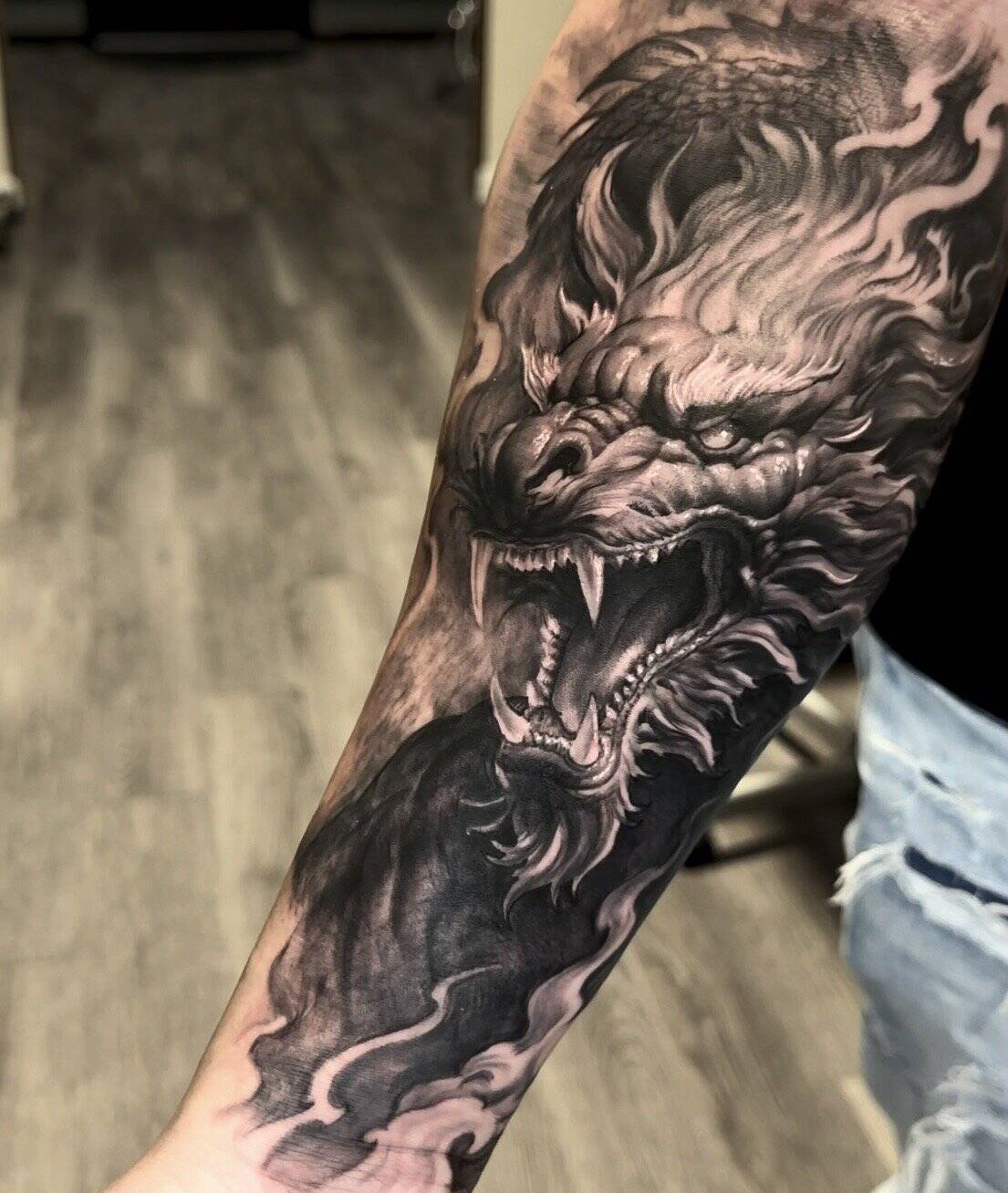 Black and grey realism forearm tattoo of a dragon head emerging from smoke