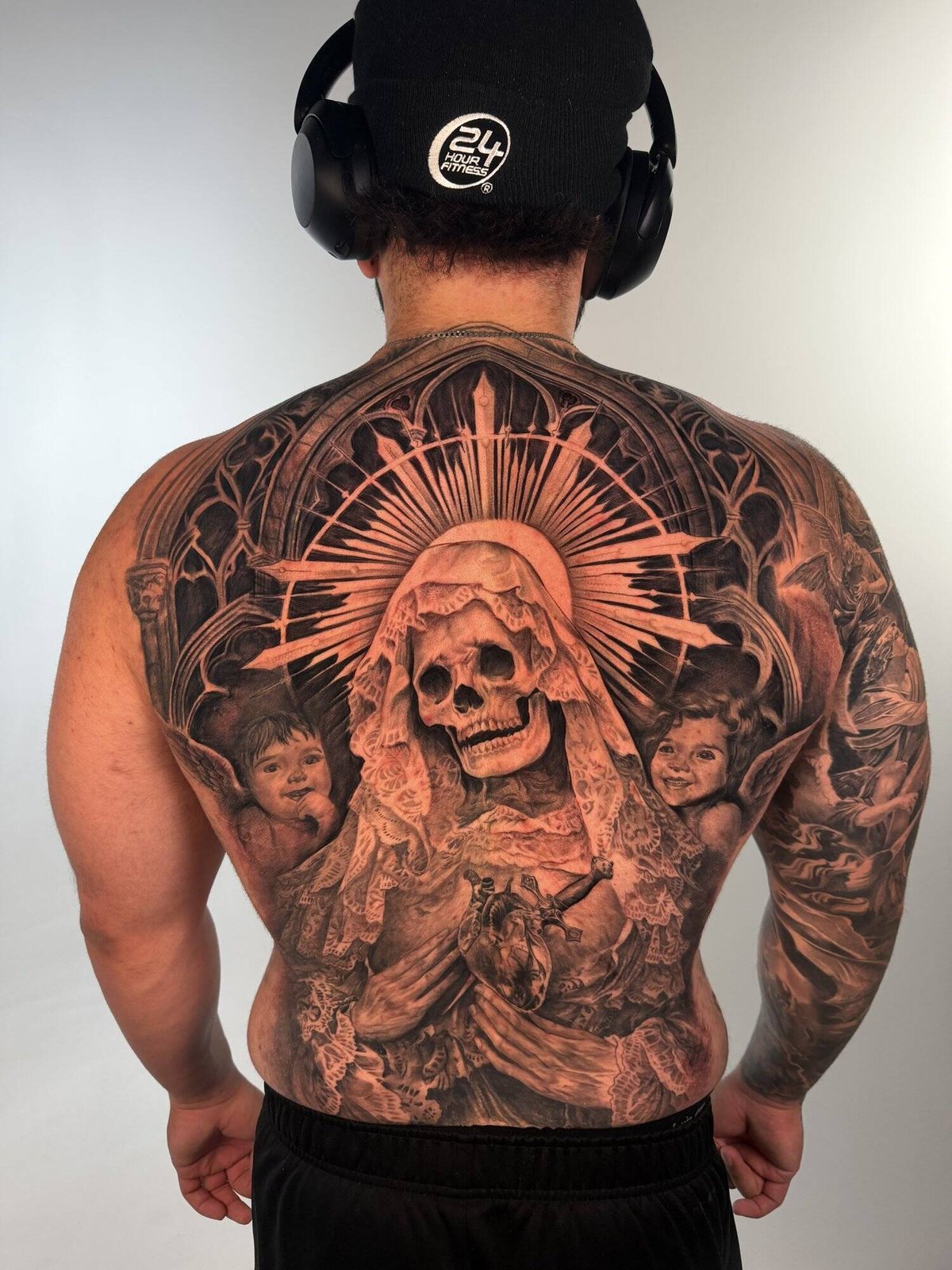 Large black and grey realism back piece of a skeletal figure beneath radiating rays, surrounded by portrait faces, covering the full back
